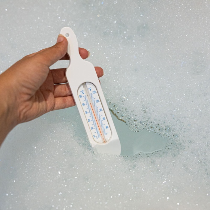 Hand holding white bath thermometer taking bath water temperature
