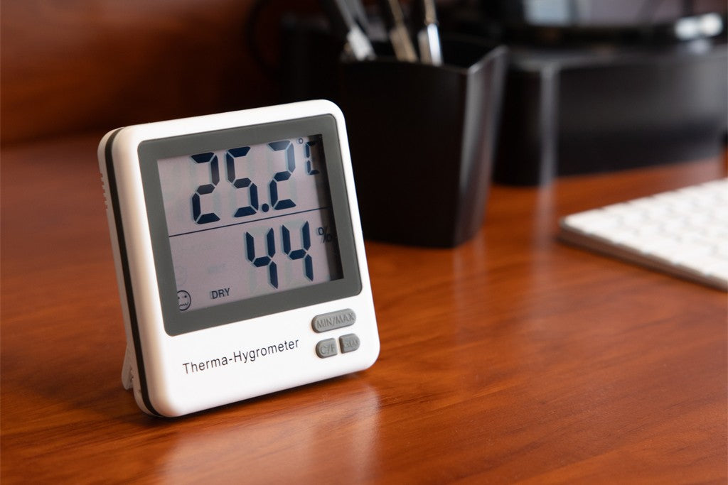A digital hygrometer on a brown wood displaying room temperature and humidity