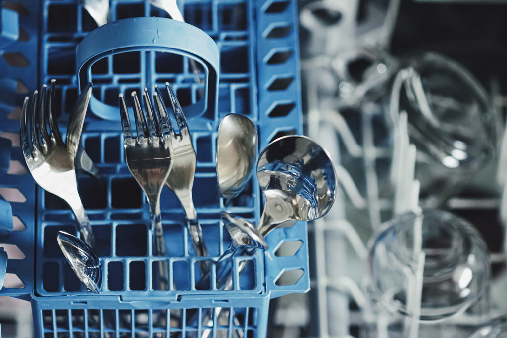 Silver cutlery in a blue commercial dishwasher tray
