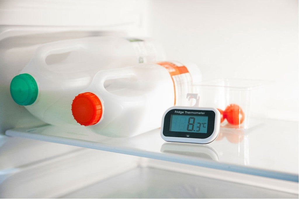 Bottles of milk, a box of cherry tomatoes and a fridge thermometer on a shelf inside a fridge