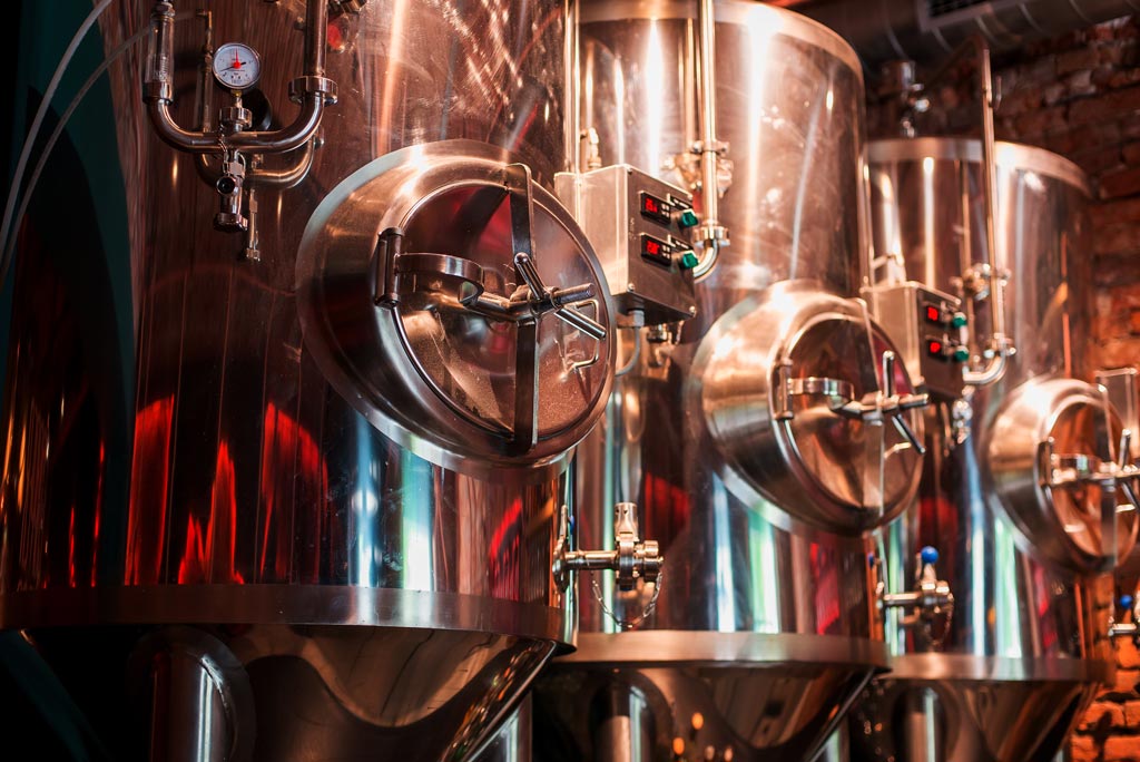 Three brass containers brewing beer in a dark room.