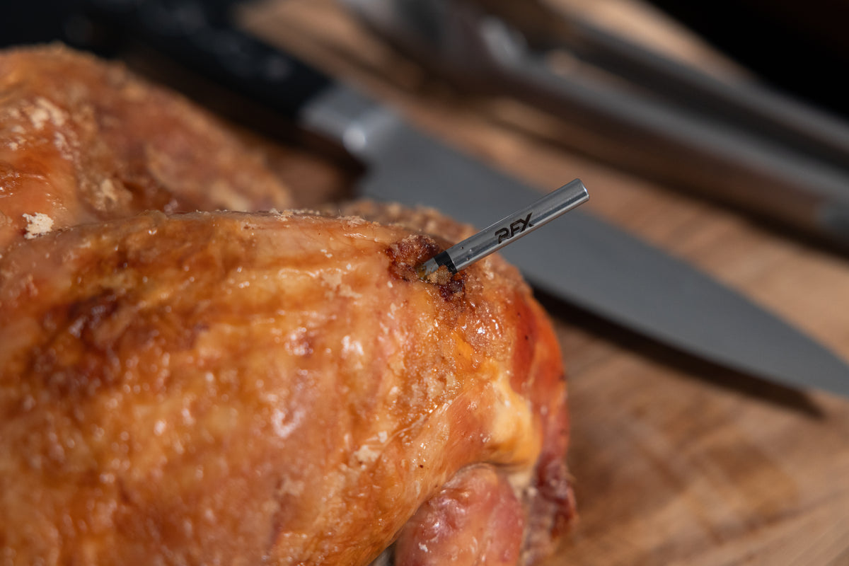 Roasted chicken with a thermometer probe inserted on a wooden cutting board.