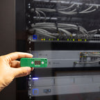 A hand holds a HumidityPod in front of a server rack with cables and blinking indicator lights.