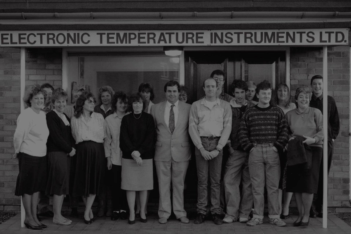 Group of people standing in front of a building with 'Electronic Temperature Instruments Ltd.' sign.