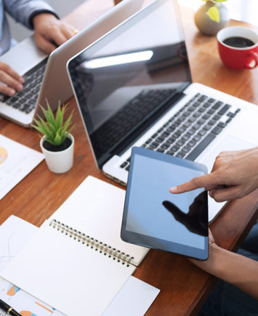 Person using a tablet with a laptop and coffee on a desk
