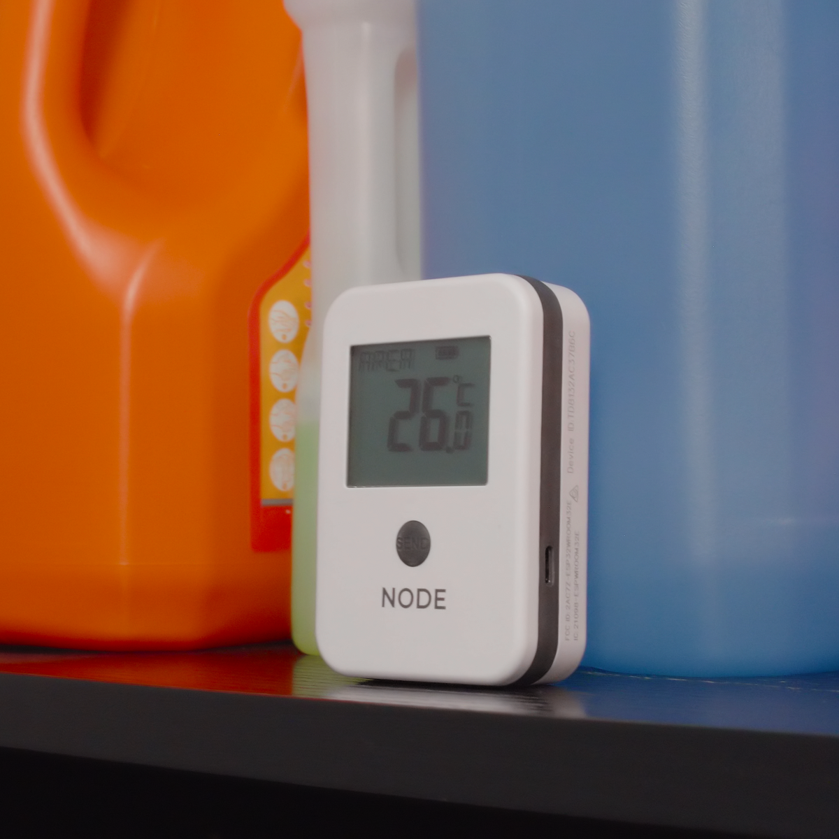 A white Node temperature sensor displaying 26 in a cleaning equipment storage cupboard.