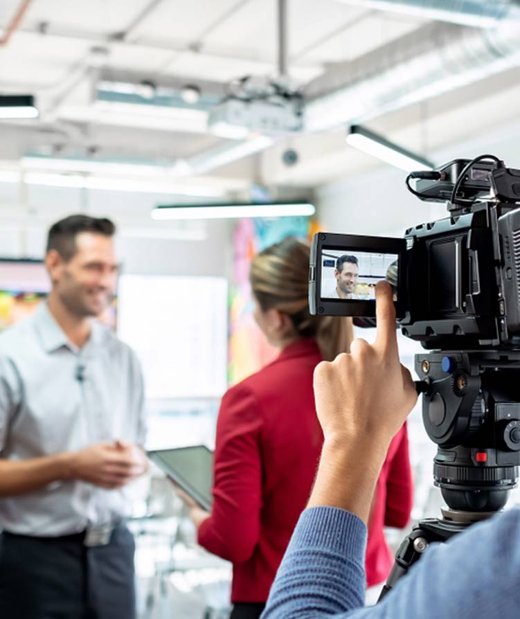 Person filming two people with a camera in an indoor setting