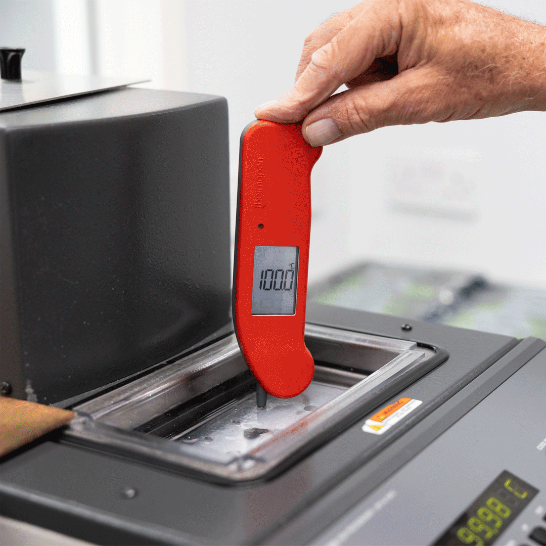 Person using a red digital thermometer on a machine with a blurred background