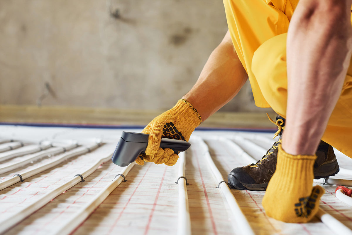 A close-up of a person testing the temperature underfloor heating pipes  using a RayTemp 8