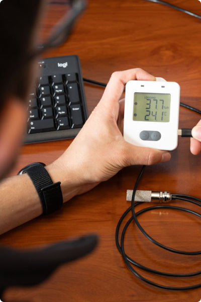 Person holding a digital thermometer on a wooden desk with a keyboard in the background