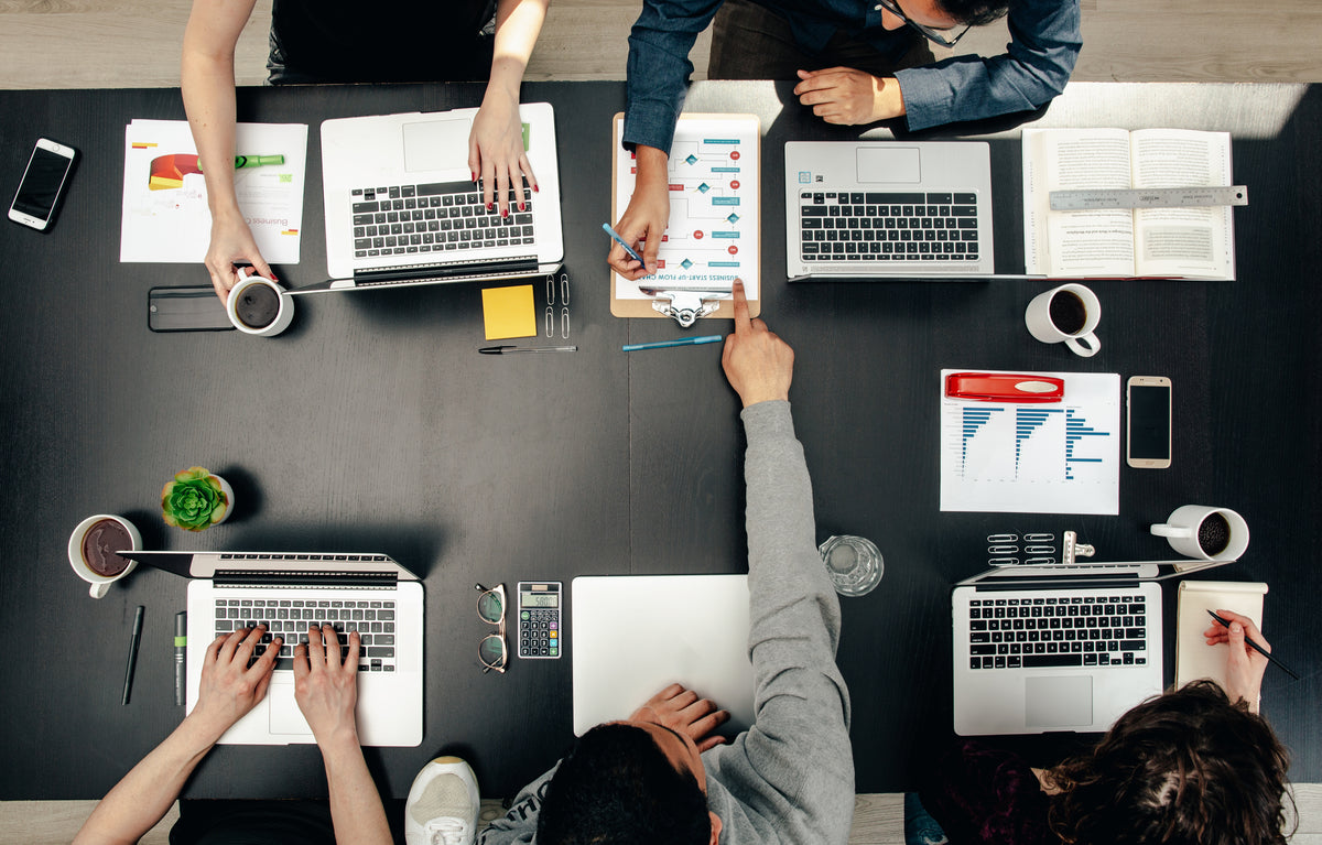 A group of people having a work meeting at a black table with laptops, notebooks and coffee