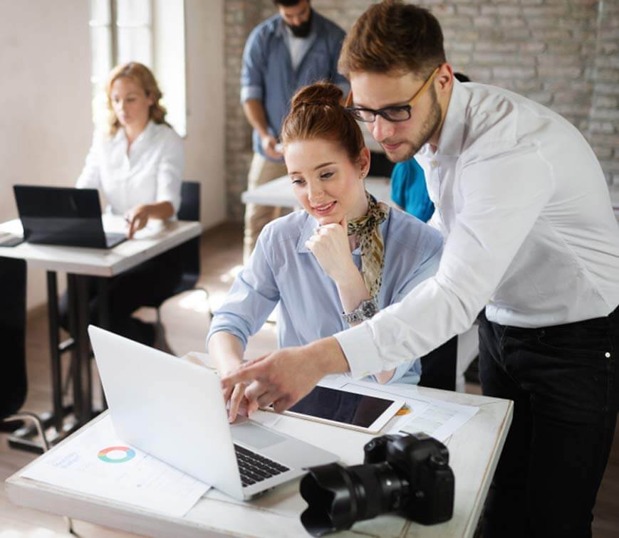 A woman and a man looking at a laptop screen man is pointing to it, office setting, two people in the background working